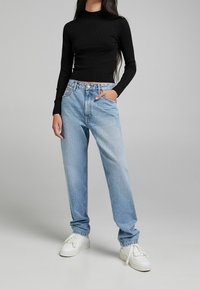 Haut noir à manches longues côtelé associé à un jean droit en denim bleu clair. Des baskets blanches complètent la tenue. Design basique et décontracté.