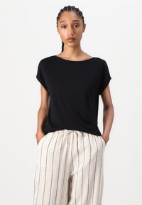 Top corto nero a maniche corte con scollatura ampia, realizzato in tessuto morbido. Abbinato a pantaloni larghi a righe beige con vita regolabile.