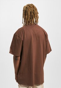 Camiseta de algodón marrón con mangas cortas y un corte relajado. Textura suave y diseño minimalista, con un escote redondeado y sin gráficos visibles.