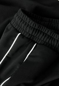 Czarne spodnie z elastycznym paskiem w talii, z białymi pionowymi paskami po bokach, wykonane z miękkiego, lekko teksturowanego materiału.