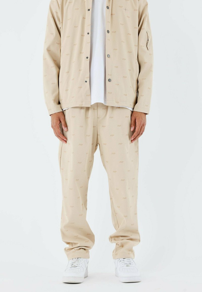 Ensemble beige en deux pièces comprenant une veste à boutons et un pantalon assorti, tous deux ornés d'un subtil motif répétitif "PXP". Des baskets blanches viennent parfaire le look.