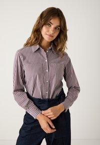 Gestreifte Button-Up-Bluse in Lila- und Weißtönen, mit klassischem Kragen, langen Ärmeln und figurbetontem Schnitt.