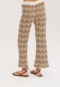 Spodnie w wzór chevron, w kolorach kremowym, czerwonym i niebieskim. Wykonane z dzianiny, z elastycznym pasem i rozszerzanym dołem.