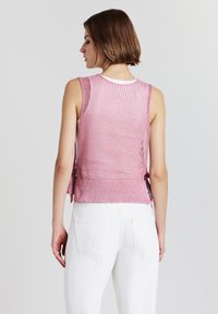Top senza maniche di un delicato rosa chiaro, realizzato a maglia con un motivo testurizzato, dotato di lacci laterali e di un colletto bianco a contrasto. Abbinato a pantaloni bianchi.