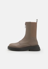 Brune lær ankle boot med ribbet elastisk side, glidelås og en solid svart såle. Glatt tekstur med enkle sømdetaljer.