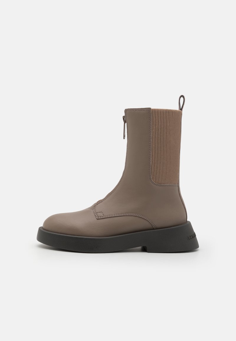 Bottine en cuir marron avec des côtés en élasthanne nervuré, fermeture éclair et une semelle noire robuste. Texture lisse avec des détails de couture simples.