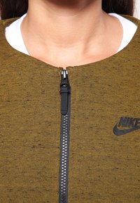 Sudadera Nike en verde oliva, con una cremallera negra y logo. Material suave con una textura moteada, cuello alto y diseño ajustado.
