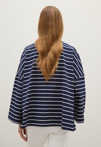 Navyblauwe en witte gestreepte oversized top met lange mouwen en een afgeronde zoom, gemaakt van een zachte stof. De achterzijde toont een relaxte pasvorm.