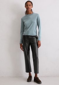 Lichtblauw languit top gecombineerd met strakke zwarte leren broek. Schoenen zijn donkerbruine suède instappers. Soepele texturen, moderne pasvorm.
