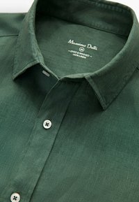 Vihreä pellavapaita, jossa on klassinen kaulus, napitus ja rento tekstuuri. Merkissä lukee "100 % pellavaa, värjätty ja pesty."