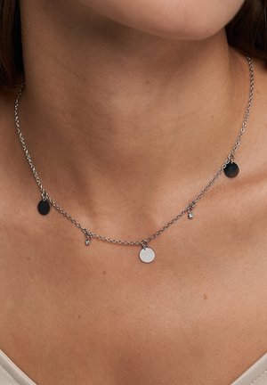 Collier chaîne en argent avec trois pendentifs circulaires en noir et argent, agrémenté d'un petit cristal mettant en valeur une texture lisse.