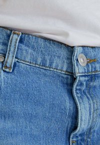 Jeans in denim blu chiaro con vita aderente, chiusura a bottone argentato e dettagli di cucitura gialla in contrasto alle cuciture.