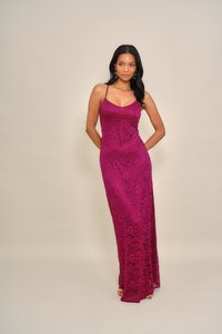 Vestido comprido justo em renda bordeaux com alças finas e decote redondo, apresentando padrões florais e uma fenda lateral. Textura suave.