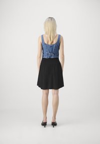 Haut en jean recadré avec un détail de nœud, associé à une jupe noire plissée. L'ensemble est présenté de dos avec un design ouvert dans le dos.