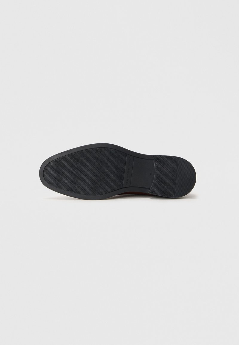 Suola di scarpa nera con una superficie texturizzata, caratterizzata da una forma liscia e arrotondata e da un logo discreto sul lato.