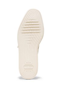 Vitt gummisul med texturerade spår och kanter. Har "Cole Haan"-logga nära hälen för identifiering.