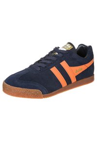 Sneaker in suede blu navy con strisce e logo arancioni, caratterizzata da una suola in gomma testurizzata e lacci piatti. Punta arrotondata e design a taglio basso.