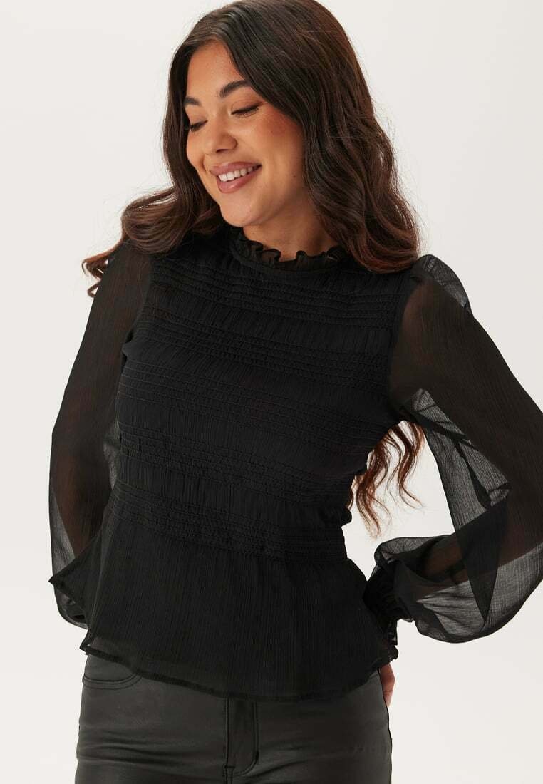 Blusa nera con maniche lunghe trasparenti, scollatura arricciata e dettagli smock sul busto e in vita. Tessuto morbido con design plissettato.