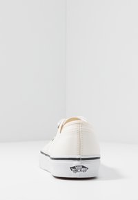 Beige Leinenschuhe mit weißen Schnürsenkeln, runder Zehenpartie und schwarzem sowie weißem Gummisohle. Mit Vans-Logo an der Ferse und kontrastierenden Nähten.