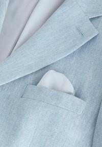 Light blue textured blazer with white silk pocket square tucked into the chest pocket and matching light blue inner lining.