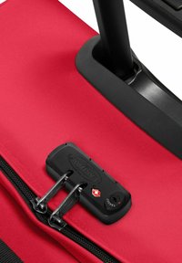 Red travel bag with a textured fabric surface, featuring a black zipper lock with two pull tabs and a TSA security keyhole.