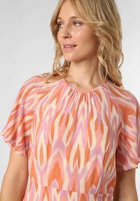 Sukienka w kwiatowy wzór w kolorze pomarańczowym, różowym i kremowym, z falbanami na rękawach i zebranym dekoltem, wykonana z lekkiej, teksturowanej tkaniny.