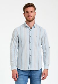 Camicia a maniche lunghe di colore azzurro chiaro con righe verticali in tonalità più scure e tessuto testurizzato. Collo e polsini con bottoni, logo sul petto.