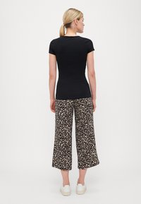 Schwarzes, figurbetontes T-Shirt kombiniert mit weit geschnittenen, beige-schwarz gepunkteten Hosen im Leopardenmuster und weißen Sneakers. Einfaches Design und lässiger Stil.