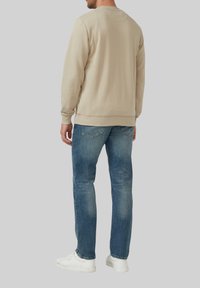 Béžová bavlnená mikina s rebrovanými manžetami a spodným lemom, v kombinácii s modrými džínsami. Celkový vzhľad dopĺňajú biele tenisky.