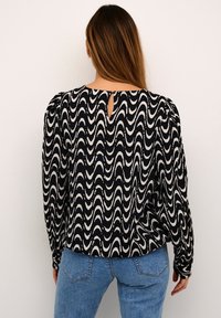 Czarnobiała bluzka w faliste wzory z długimi rękawami, puffed shoulders i dekoltem w kształcie otworu z tyłu, w połączeniu z jasnoniebieskimi dżinsami.