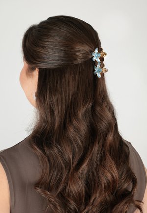 Capelli lunghi castano scuro, mossi, metà raccolti con due mollette blu a forma di fiore, visti da dietro.