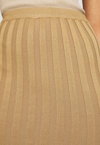 Béžová pletená sukně s vertikálními pruhy, s elastickým pasem a hladkou texturou. Látka má mírný lesk.