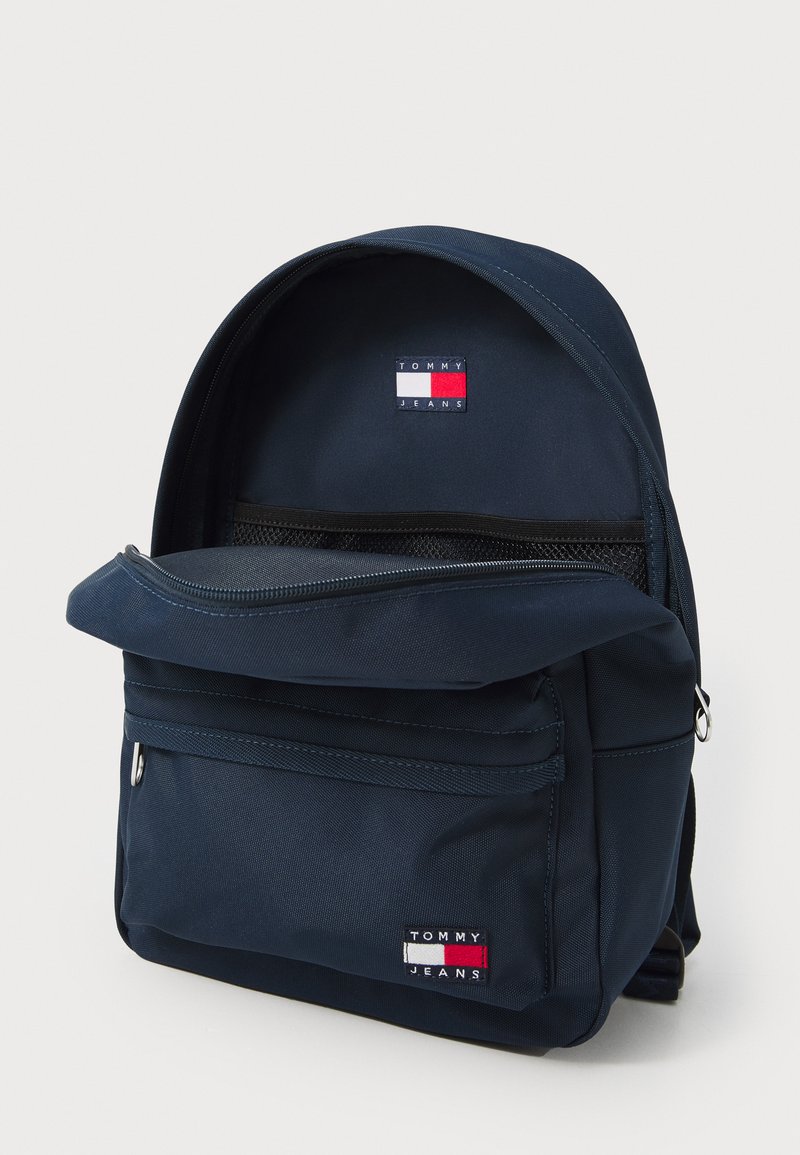 Granatowy plecak wykonany z trwałego materiału, z zamykaną na zamek kieszenią z przodu, naszywką z logo oraz teksturowanym materiałem.