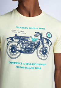 Svetle žluté tričko s grafikou motocyklisty v modré barvě, se textem "Hawaiian Kahua Trail" a "Petrol" v tučném písmu.
