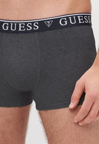 Boxeri din bumbac gri, cu un tiv elastic negru pe care se află inscripția albă "GUESS". Textură netedă, design ajustat, cu detalii de cusătură vizibile.