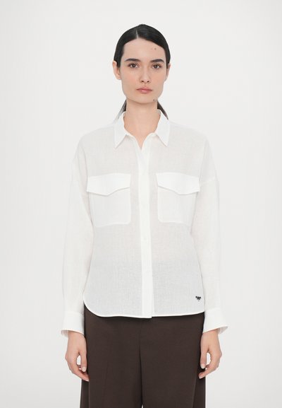 Chemise blanche à boutons, fabriquée en lin léger, avec deux poches avant, coupe régulière et ourlet arrondi. Dispose d'un détail logo discret.