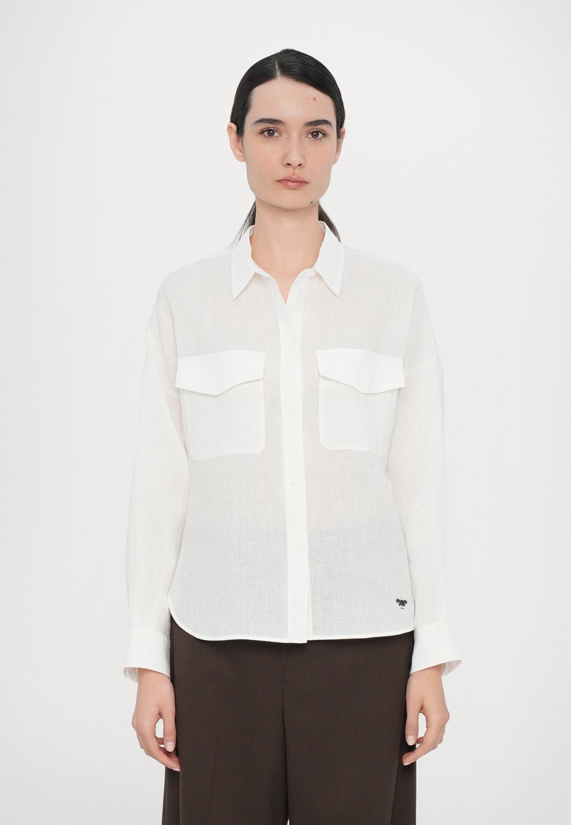 White button-up shirt made of lightweight linen with two front pockets, regular fit, and a rounded hem. Features subtle logo detail.