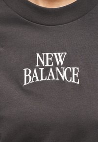 Σκούρο γκρι φούτερ με ριμπ λαιμόκοψη και λευκό κεντημένο λογότυπο "NEW BALANCE" στο κέντρο του στήθους. Μαλακή υφή υφάσματος.