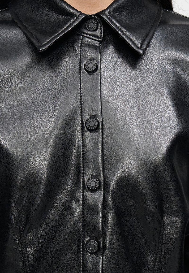 Chemise en cuir noir avec col pointu, fermeture avant à boutons ronds noirs, et texture lisse.