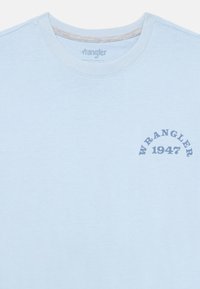 Šviesiai mėlynas medvilnės marškinėliai su apvaliu iškirpimu. Priekyje yra tamsiai mėlynas grafikas "WRANGLER 1947". Minkšta tekstūra, kasdienis dizainas.