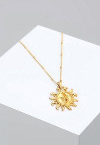 Goldanhänger mit einem Sonnendesign, das ein detailliertes Gesicht und hervortretende Strahlen zeigt, hängt an einer zarten Kette.