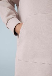 Hellrosa Kapuzenpulli mit gerippten Bündchen und einer Fronttasche. Der Stoff hat eine glatte Textur mit einer dezenten Nahtdetail.