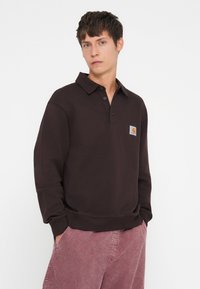 Dark brown polo sweatshirt with long sleeves, buttoned collar, and a chest label featuring a logo. Soft fabric with a relaxed fit.