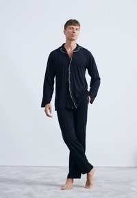 Conjunto de pijama negro que incluye una camisa de botones con un cuello blanco y pantalones. Tela suave con un corte relajado y mangas largas.
