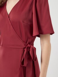 Burgundy kietaisdress, joka on valmistettu sileästä kankaasta ja jossa on lyhyet liehuvat hihat, V-mallinen kaula-aukko ja sivussa solmittava yksityiskohta vyötäröllä.