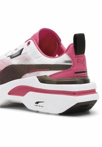 Sneakers Puma z białą siateczkową cholewką, różowymi akcentami, przezroczystą częścią pięty oraz teksturowaną białą podeszwą środkową z czarnymi detalami.