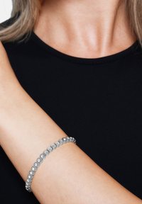 Pulsera de plata con eslabones circulares y pequeñas piedras incrustadas. Lleva en una muñeca desnuda, contrastando con una blusa negra.