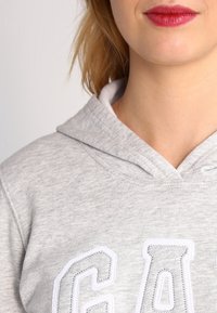 Sudadera con capucha gris, con un acabado texturizado y un destacado logo bordado en blanco en la zona del pecho.