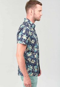 Camisa de manga corta, con botones, en navy oscuro con un patrón floral en blanco y azul claro. Tejido ligero con un corte relajado y diseño de cuello.