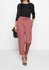 Roze, losse broeken met een elastische tailleband en koord. Gecombineerd met een zwarte, lange mouwen top en zwarte, strap sandaaltjes.